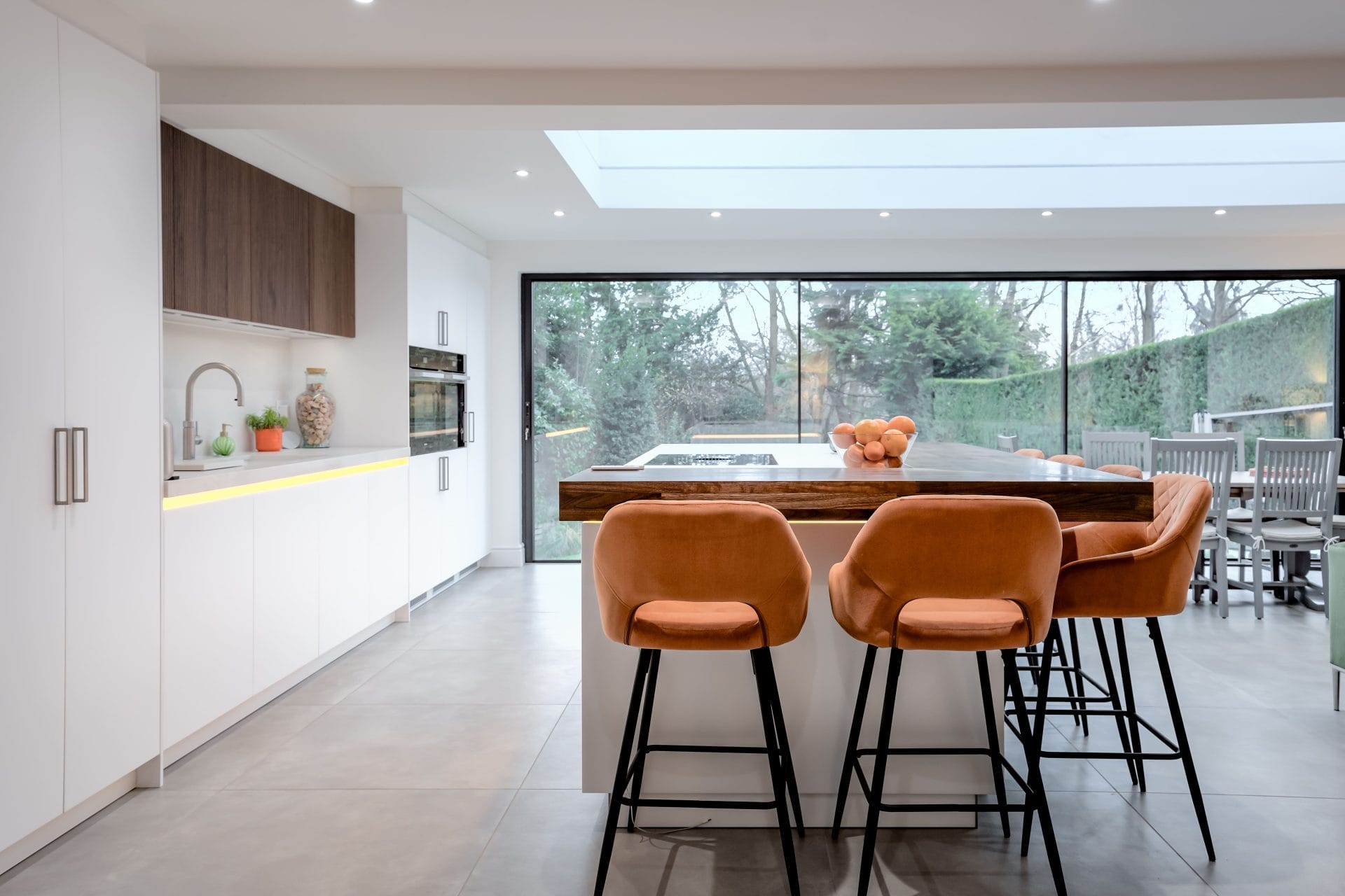Modern white and walnut kitchen with breakfast bar seating and large sliding glass doors