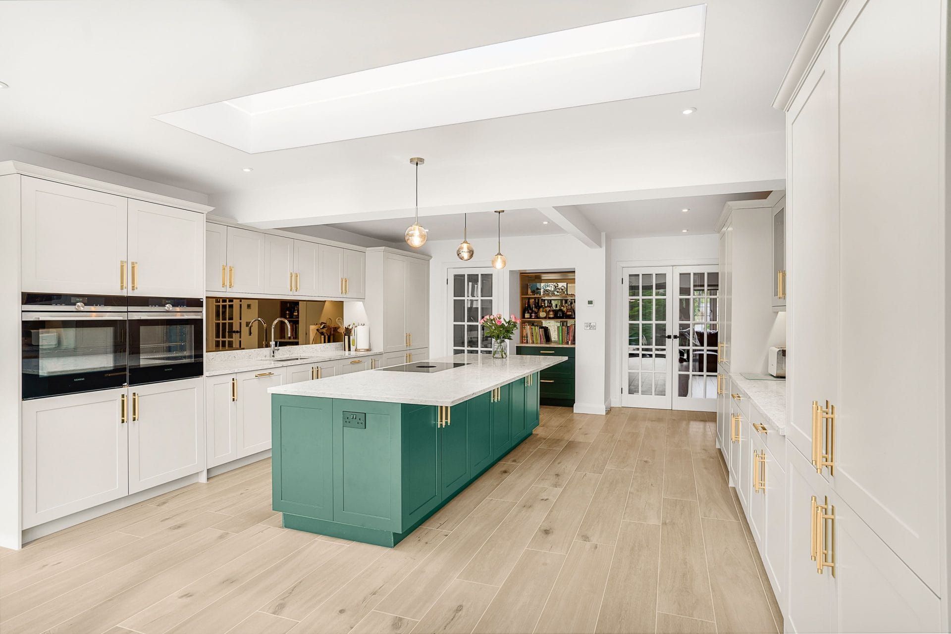 Spacious shaker style kitchen with green island, marble worktop and pendant lighting in an open plan layout