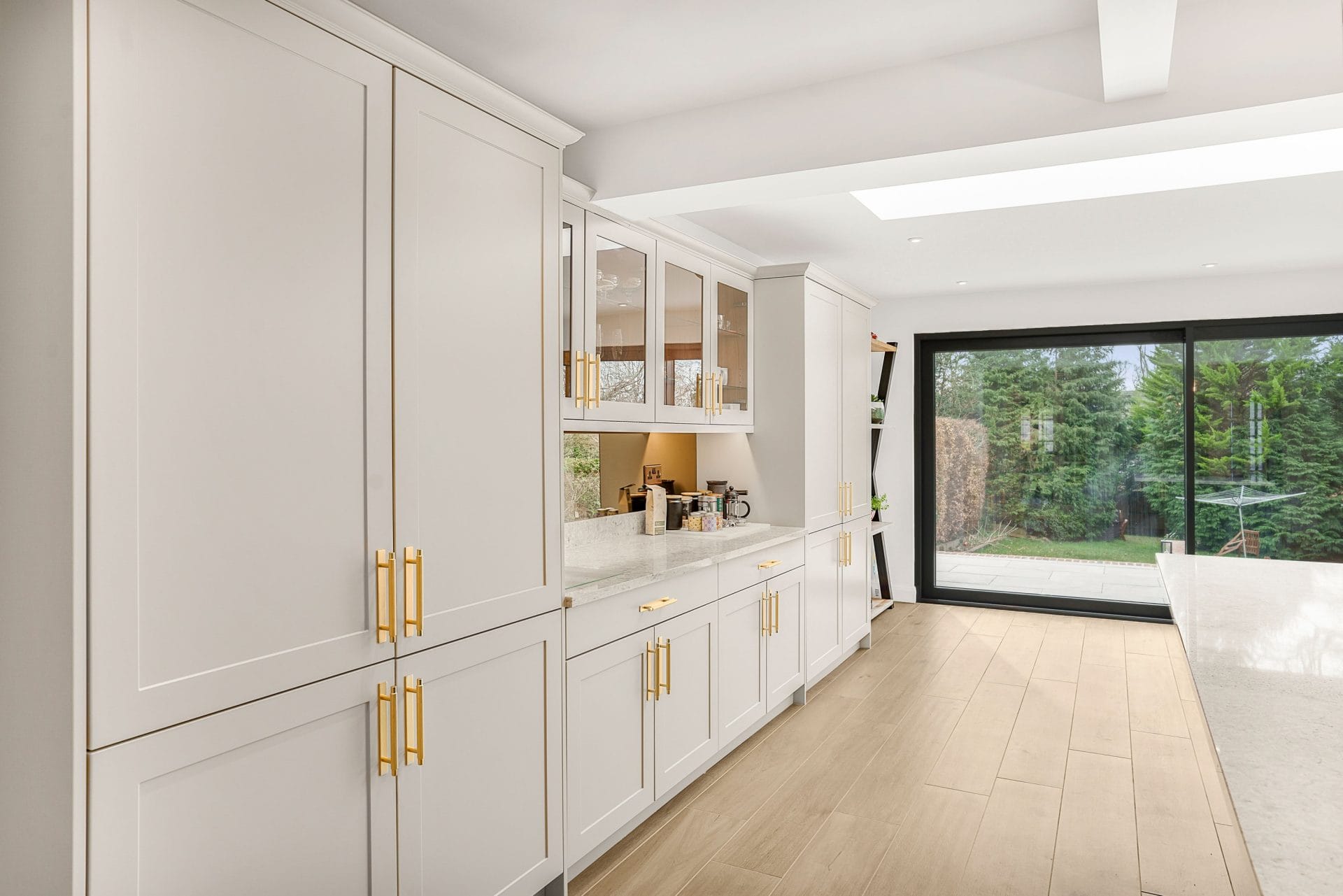 Modern light shaker kitchen with tall cabinetry, gold handles and large sliding patio doors